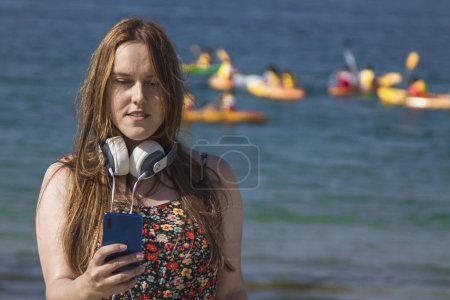 Téléchargez les photos : Femme souriante sur la plage avec téléphone et écouteurs - en image libre de droit