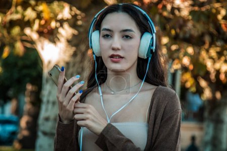 Photo for Young woman with headphones listening to a podcast on autumn background - Royalty Free Image