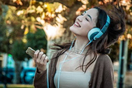 Photo for Young woman with headphones dancing on autumn background - Royalty Free Image