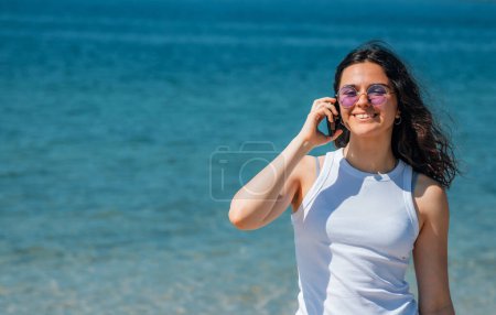 Mädchen lächelt glücklich mit Smartphone am Strand