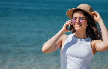 Mädchen lächelt glücklich mit Smartphone am Strand