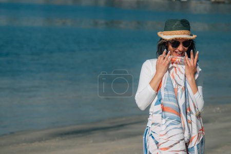 lächelnde junge Frau am Strand in sommerlichem Modetrend-Outfit unbeschwert und glücklich, Freiheitsgefühl, Boho-Chic und Sonnenbrille
