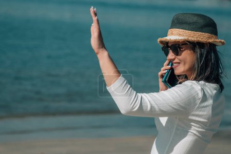 Téléchargez les photos : Jeune femme avec téléphone portable sur la plage et dire bonjour - en image libre de droit