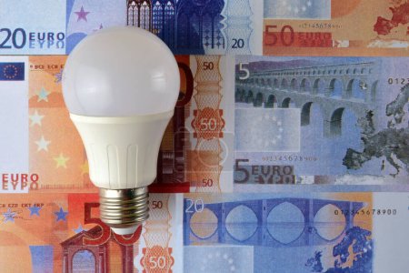 Foto de Una bombilla led de bajo consumo sobre un fondo de billetes en euros - Imagen libre de derechos