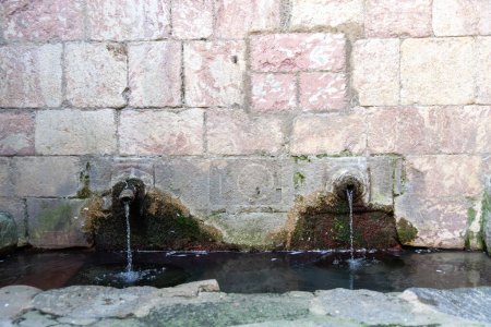 Photo for Two old water outlets of a spring in a wall, from which water is constantly flowing. Around the taps you can see corrugated surfaces on the wall and a small basin in which the water is collected - Royalty Free Image