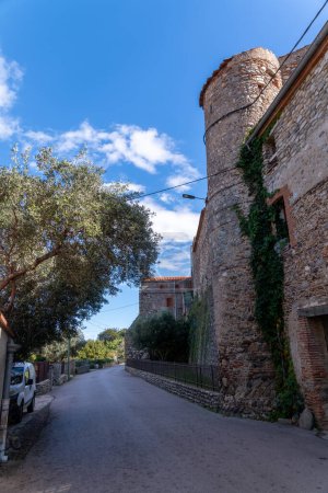 Photo for Idyllic road under a blue sky with old houses on the right and trees on the left. The road bends to the right further on - Royalty Free Image