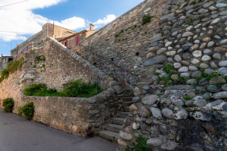 Foto de Una escalera de piedra que sube por una pared de piedra con edificios en la parte superior. Hay mucha vegetación en la pared y las escaleras y las piedras están parcialmente hechas de piedra natural y piedras talladas. - Imagen libre de derechos