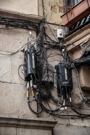 Téléchargez les photos : De nombreux câbles téléphoniques noirs sur un mur de la maison, qui finissent désorganisés et enchevêtrés dans des boîtes de jonction. Certains des câbles sont étiquetés. C'est un défi pour tout technicien - en image libre de droit