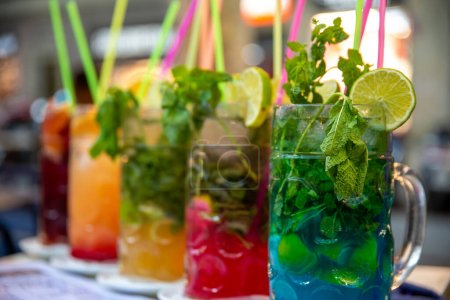 Photo for Several different large jugs with different drinks, which are also different colors. The drinks are decorated with limes and herbs. There are straws in each glass. - Royalty Free Image