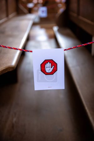 Foto de Un signo blanco colgado en una cuerda con un símbolo de una mano en un hexágono rojo. La señal está destinada a indicar que los bancos detrás de ella no se pueden utilizar. - Imagen libre de derechos