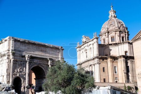 Foto de Roma, Lacio - Italia - 23-11-2022: El Arco de Septimio Severo y a la derecha la iglesia de Santi Luca e Martina, con columnas en dos niveles en su fassade. La iglesia tiene una gran cúpula en su techo - Imagen libre de derechos