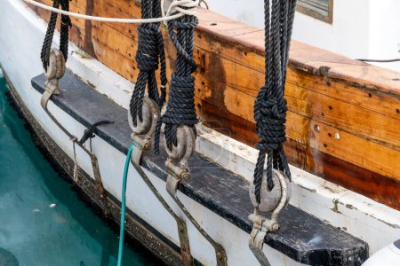 Téléchargez les photos : Cartagena, Murcie - Espagne - 16-01-2024 : Gros plan sur le gréement traditionnel du voilier, avec cordes nouées, anneaux en bois et câbles en acier tendus contre la coque en bois - en image libre de droit