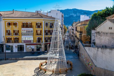 Photo for Denia, Alicante - Spain - 12-22-2023: Main street in Denia, Spain, featuring festive lights and a mountain backdrop, with locals strolling - Royalty Free Image