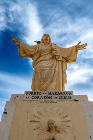 Puerto de Mazarron, Murcia - Spain - 01-18-2024: Statue of Jesus with open arms atop a pedestal in Puerto de Mazarron, against a cloudy sky