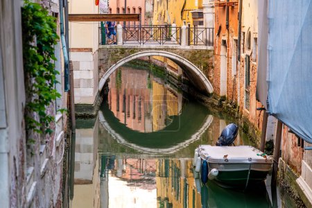 Photo for Venice, Veneto - Italy - 06-10-2021: Calm water mirrors an arched bridge in a peaceful Venetian alleyway - Royalty Free Image