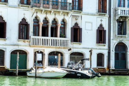 Téléchargez les photos : Venise, Vénétie - Italie - 06-10-2021 : Elégant bâtiment vénitien avec fenêtres cintrées donnant sur le Grand Canal, avec des bateaux à moteur amarrés devant lui. - en image libre de droit