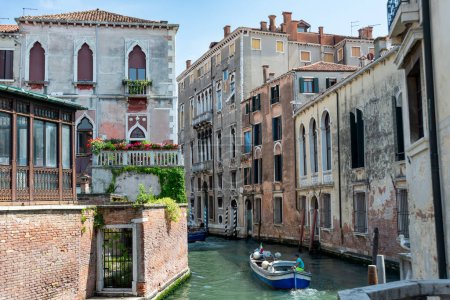 Téléchargez les photos : Venise, Vénétie - Italie - 06-09-2021 : Bateau navigue doucement à travers un canal calme bordé d'architecture vénitienne historique - en image libre de droit