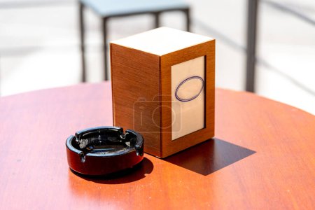 Vicenza, Venetien - Italy - 06-12-2021: A wooden napkin dispenser beside an empty ceramic ashtray on a sunlit cafe table in Vicenza