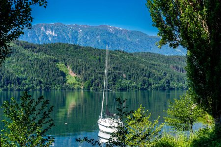 Millstatt am See, Kaernten - Austria - 06-16-2021: Millsttter Lake: An anchored sailboat floats on a tranquil Austrian lake, framed by alpine mountains and trees