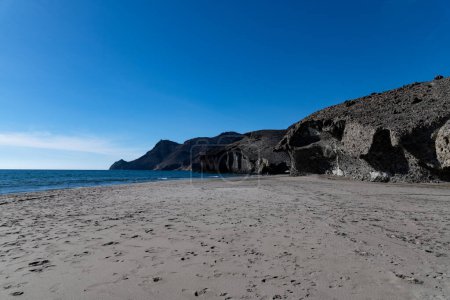 Cabo de Gata, Almeria - Spanien - 23-01-2024: Sandstrand von Cabo de Gata unter klarem blauem Himmel, mit schroffen Klippen am Rande des ruhigen Meeres