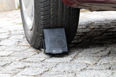 Bautzen, Sachsen - Deutschland - 04.10.2021: Autoreifen fest mit einem schwarzen Keil auf einer grau strukturierten Straßenoberfläche eingeklemmt