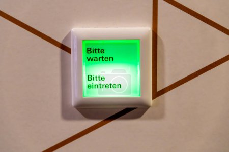 Bautzen, Sachsen - Deutschland - 04.10.2021: Ein grün beleuchtetes Schild mit "Bitte warten" und "Bitte eintreten", das auf Warte- und Einreisehinweise hinweist