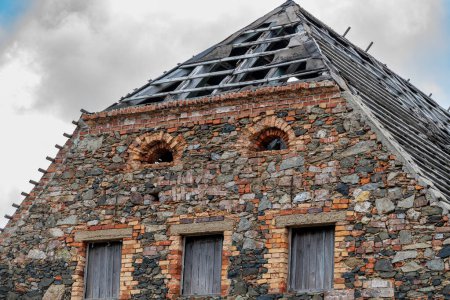 Ossig, Sachsen - Deutschland - 18.04.2021: Giebelblick eines alten Bauernhauses mit Feldsteinmauern, drei rechteckigen und zwei kleinen halbrunden Fenstern und einer ziegellosen Dachkonstruktion