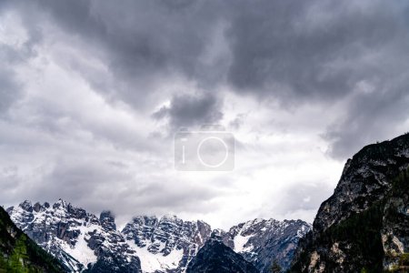 Alpen, South Tyrol - Italy - 06-07-2021: Close-up of dark clouds looming over partly snow-covered mountain peaks in the Alps, creating a dramatic scene