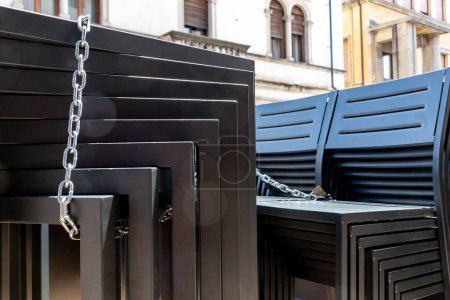 Téléchargez les photos : Vicenza, Venetien - Italie - 06-12-2021 : Des bancs modernes noirs empilés créant des motifs géométriques ornés et fixés avec une chaîne et un cadenas. - en image libre de droit