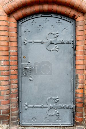 Foto de Loebau, Sajonia - Alemania - 17-04-2021: Puerta de hierro con bisagras decorativas y patrones de trébol, colocada en un arco de ladrillo - Imagen libre de derechos