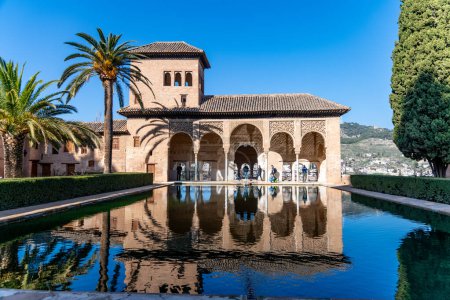 Foto de Granada, Granada - España - 30-01-2024: Reflejo del Palacio El Partal en su cuenca hidrográfica, rodeado de palmeras bajo un cielo azul - Imagen libre de derechos