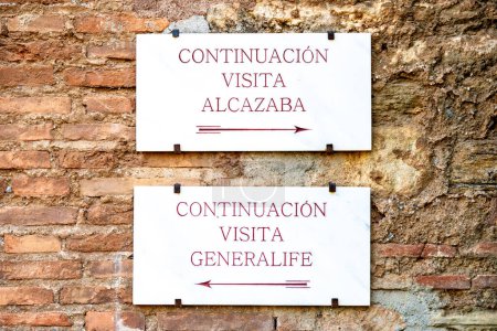 Foto de Granada, Granada - España - 30-01-2024: Carteles blancos con letras rojas y flechas que apuntan a Alcazaba y Generalife en la Alhambra guían a los visitantes a través de maravillas históricas - Imagen libre de derechos