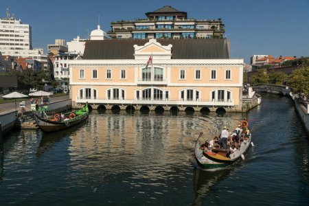 Téléchargez les photos : AVEIRO, PORTUGAL - 30 AOÛT 2019 : Ancien bâtiment de capitainerie dans le canal central d'aveiro avec les bateaux moliceiro traditionnels, Région de Beira, Portugal. - en image libre de droit