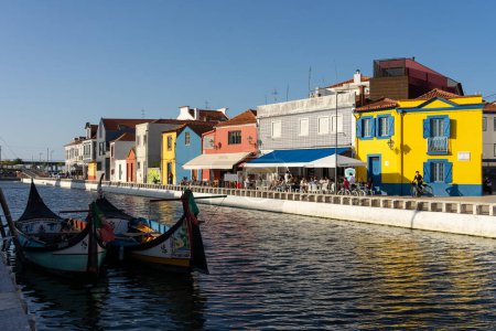 Foto de AVEIRO, PORTUGAL - 30 de agosto de 2019: Cais dos Botiroes y la Casa do Mercado amarilla en uno de los canales de Aveiro con las típicas casas y barcos moliceiros al atardecer, región de Beira, Portugal - Imagen libre de derechos