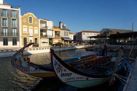 Foto de AVEIRO, PORTUGAL - 30 de agosto de 2019: Cais dos Botiroes y la Casa do Mercado amarilla en uno de los canales de Aveiro con las típicas casas y barcos moliceiros al atardecer, región de Beira, Portugal - Imagen libre de derechos