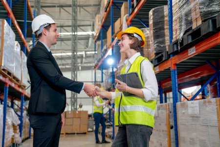 Photo for Manager shake hands with warehouse factory worker woman who hold tablet and express happiness with smiling and they stay in front other worker check the product in the back - Royalty Free Image