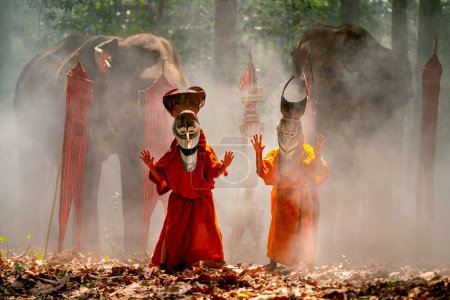 Photo for Two boy wear Pee Ta Khon, traditional culture art as ghost of Asian culture, dress and look at camera and elephants stand in the background and they stay in forest. - Royalty Free Image