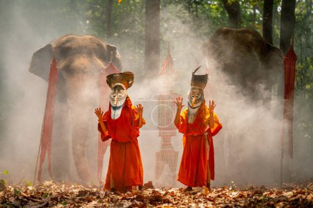 Photo for Two boy wear Pee Ta Khon, traditional culture art as ghost of Asian culture, dress and action to show horror position and elephants stand in the background and they stay in forest. - Royalty Free Image