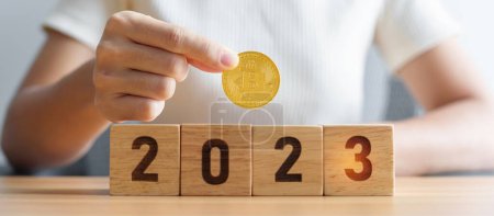 Hand hält goldene Bitcoin oder BTC Kryptowährung über 2023 Jahre Blöcke. Krypto-Handel, Digitalgeld, Blockchain und Neujahrskonzepte