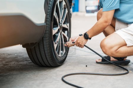 Photo for Man driver hand inflating tires of vehicle, removing tire valve nitrogen cap for checking air pressure and filling air on car wheel at gas station. self service, maintenance and safety - Royalty Free Image