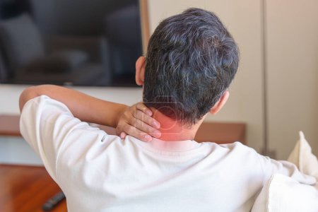 Mann mit Nacken- und Schulterschmerzen beim Sitzen auf Sofa. aufgrund von Fibromyalgie, Rheuma, Skapulierschmerzen, Bürosyndrom und ergonomischem Konzept
