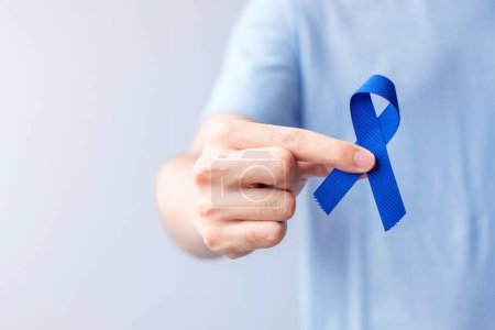 Téléchargez les photos : Mars Mois de sensibilisation au cancer colorectal, Femme tenant un ruban bleu foncé pour soutenir les personnes vivant et malades. Santé, espoir et concept de Journée mondiale contre le cancer - en image libre de droit