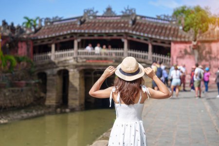 Téléchargez les photos : Femme voyageuse visitant le pont couvert japonais ou le temple Cau à Hoi Une ville ancienne, au Vietnam. repère et populaire pour les attractions touristiques. Vietnam et Asie du Sud-Est concept de voyage - en image libre de droit