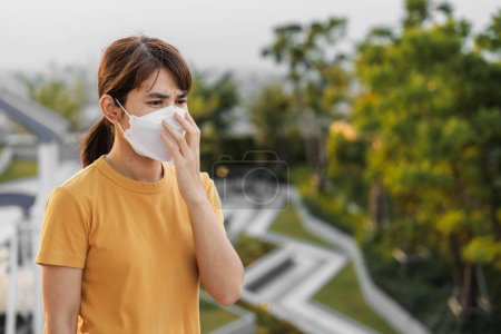 Téléchargez les photos : Jeune femme asiatique portant un masque respiratoire N95 protéger et filtrer pm2.5 ou particules contre la pollution atmosphérique mauvaise dans la ville. Indice de Qualité de l'Air, IQA, Malsain, concept de soins de santé - en image libre de droit