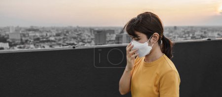 Foto de Mujer asiática joven que usa máscara respiratoria N95 protege y filtra pm2.5 o partículas contra la mala contaminación del aire en la ciudad. Índice de Calidad del Aire, ICA, Insalubre, concepto de salud - Imagen libre de derechos