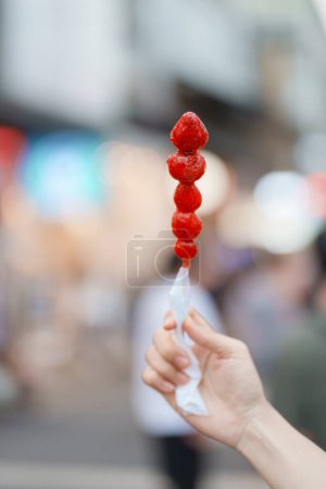 Photo for Woman hand holding caramel coated strawberry skewer at night market. Street Food and travel concept - Royalty Free Image