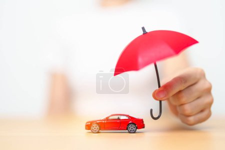Photo for Businesswoman hand holding red umbrella and cover red car toy on table. Car insurance, warranty, repair, Financial, banking and money concept - Royalty Free Image