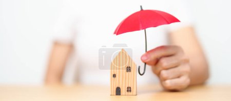 Téléchargez les photos : Femme d'affaires main tenant rouge couverture de parapluie en bois modèle maison. concepts immobiliers, d'assurance et de propriété - en image libre de droit