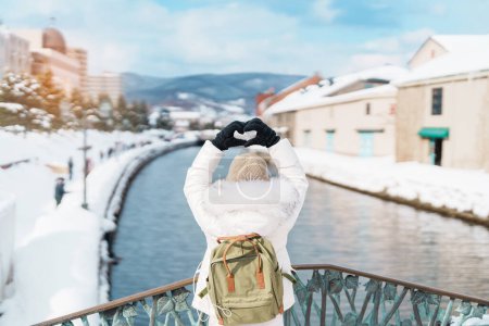 Touristin zu Besuch in Otaru, glückliche Reisende im Pullover besichtigen Otaru Kanal mit Schnee in der Wintersaison. Wahrzeichen und beliebt für Attraktionen in Hokkaido, Japan. Reise- und Urlaubskonzept