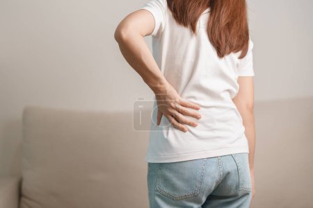 Photo for Woman having back body ache during sitting on Couch at home. adult female with muscle pain due to Piriformis Syndrome, Low Back Pain and Spinal Compression. Office syndrome and medical concept - Royalty Free Image